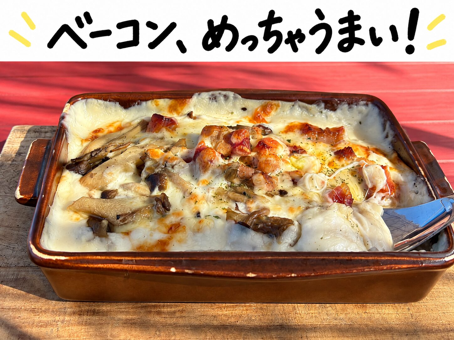 赤いテーブルに置かれたキノコとベーコンのグラタンドリア